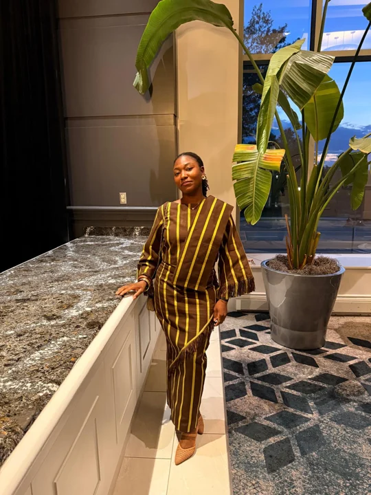 A convention guest in a brown and gold striped outfit posing beside a tall indoor plant